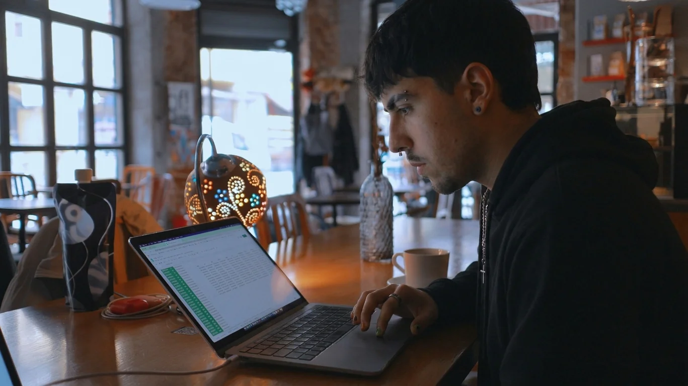 Programador trabajando en su portátil en una cafetería, con la pantalla mostrando código y un café al lado